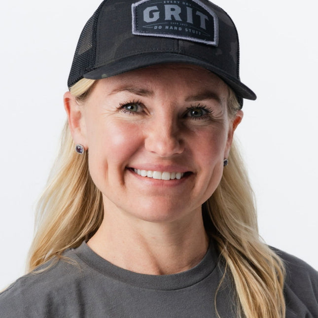 Woman smiling in GRIT Hat Magic Camo from Do Hard Stuff – gear for those who never give up