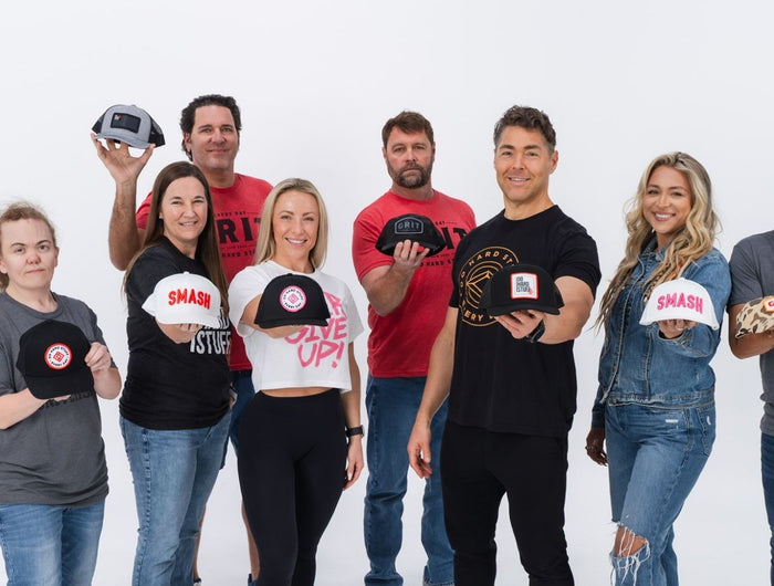 A diverse group of real people wearing Do Hard Stuff apparel, holding out hats as a symbol of strength, perseverance, and community,