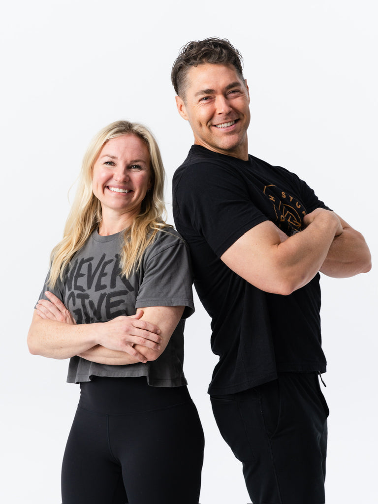Two smiling individuals in Do Hard Stuff apparel, standing strong with arms crossed, representing perseverance and a never-give-up mindset.