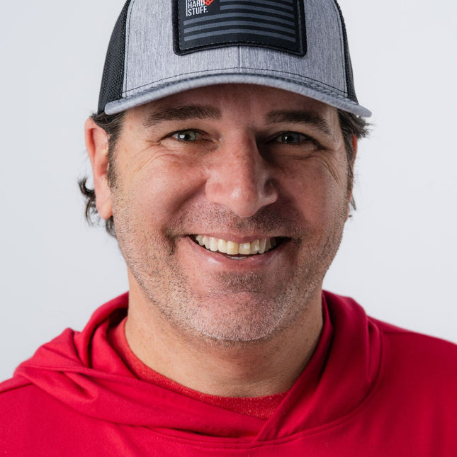 Man wearing heather gray Do Hard Stuff Patriot Hat with black mesh and patch logo, smiling directly at camera.