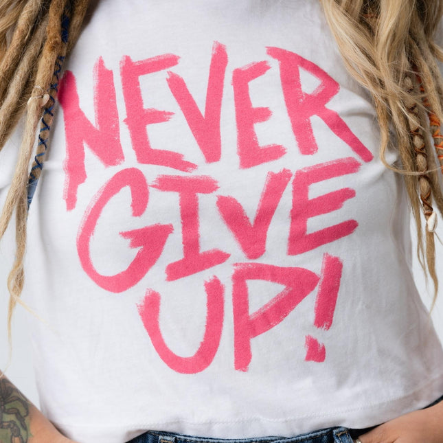 Close-up of the pink "Never Give Up!" text on the white Do Hard Stuff crop tee.