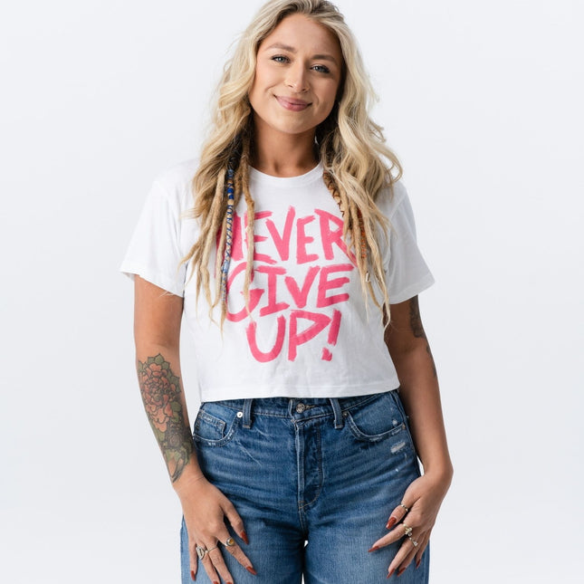 Woman smiling while wearing the Do Hard Stuff pink and white crop tee with "Never Give Up" message.