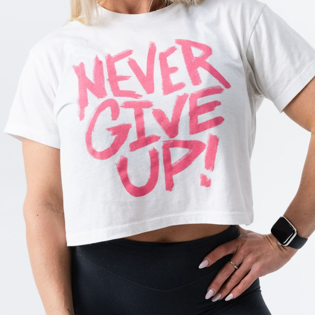 Confident pose with hand on hip in the pink and white "Never Give Up" crop tee.