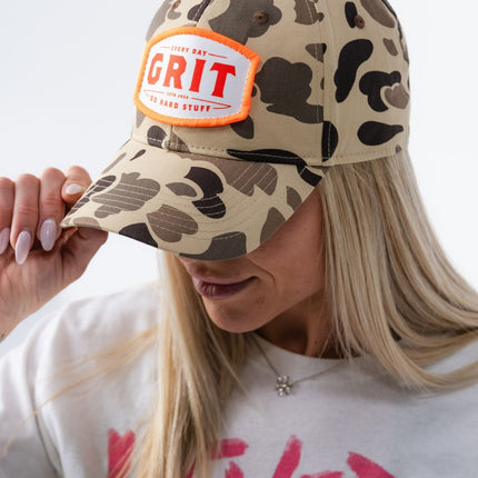 Profile view of woman wearing vintage camo Grit Hat with bold orange-trimmed patch