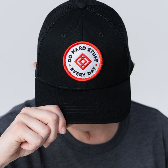 Woman tilting the black Inner Circle Hat downward, showing the front logo clearly.