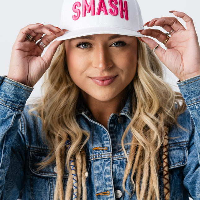 Close-up of woman holding the brim of her Pink Smash Hat with both hands, smiling confidently.