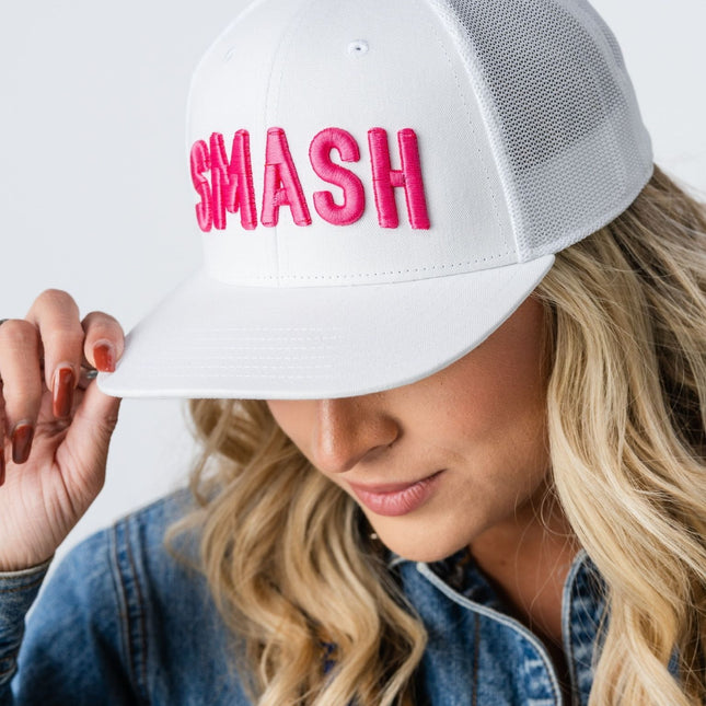 Woman smiling while wearing the Pink Smash Hat, front facing with logo visible.