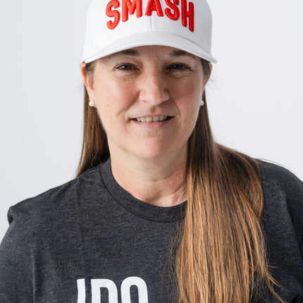 Woman adjusting the white Smash hat with orange letters from Do Hard Stuff, wearing a dark graphic tee.